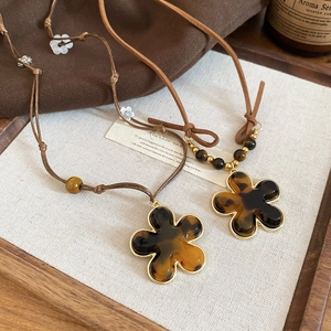 Close-up of tortoise shell resin flower pendant with gold trim on brown cord