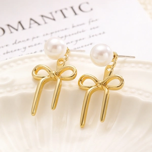 Detail shot of golden ribbon bow earrings with round white pearls on a romantic tray