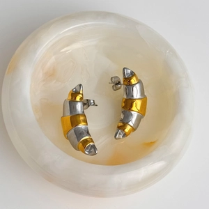 Minimalist two-tone gold and silver croissant stud earrings on marble stone tray