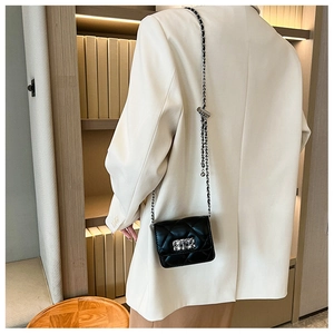 Close-up of a black quilted crossbody bag with a gold chain strap on a beige blazer