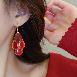 Detail of red layered waterdrop tassel earrings worn by a model on a beige background