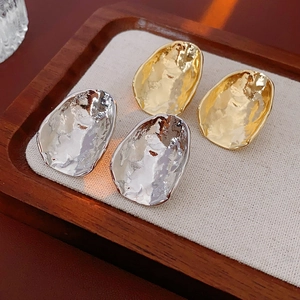 Detail of gold and silver irregular hammered metal stud earrings on a beige linen display