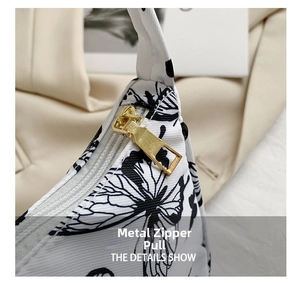Close-up of golden metal zipper and butterfly print on a stylish white shoulder bag
