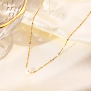 Close-up of a glossy white pearl pendant on a delicate gold chain against silk fabric