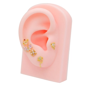 Detail view of five gold piercings with pink crystals on a model ear model