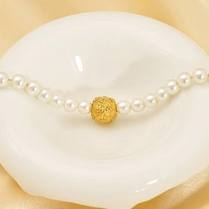 Elegant pearl necklace with textured gold bead on white ceramic plate with gold satin