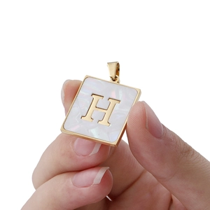 Golden 22mm square pendant with white shell inlay and letter H held by hand