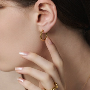 Gros plan de boucles d'oreilles créoles dorées en acier titane portées par un mannequin