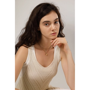 Detail of a layered golden heart necklace on model wearing cream knit vest