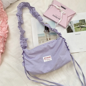 Detail of light purple pleated shoulder bag with ruffled strap and brand label on white bed