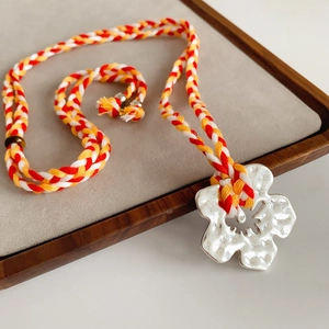 Macro view of handmade silver flower pendant on a red and yellow woven cord necklace