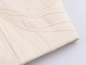 Macro detail showing cream twill cotton fabric with precise wave pattern embroidery stitches
