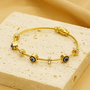 Detail of gold-toned twisted wire bracelet with Evil Eye charm on travertine stone