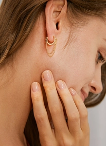 Detailed close-up of golden hoop earrings with delicate double tassel chains on a model