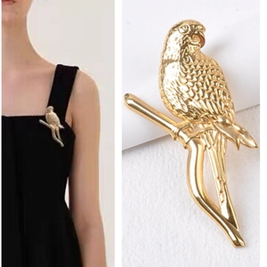 Detail view of a gold-colored bird brooch on a branch shown on a model and close-up
