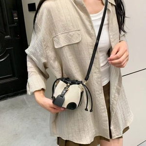 Close-up of a mini beige canvas drawstring bucket bag with black leather trim and strap