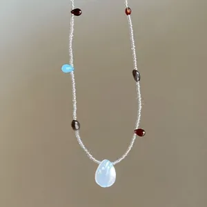 Close-up of beaded necklace with colorful teardrop gemstones and white focal stone