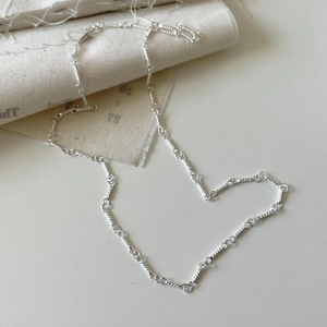 Detailed close-up of 925 sterling silver twist chain necklace on a rustic texture cloth