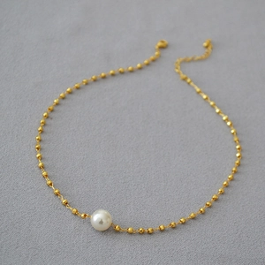 Detailed close-up of a white pearl necklace with gold-plated beaded brass chain links