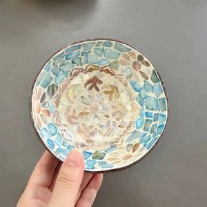 Detail of a handmade coconut bowl with blue and beige shell mosaic floral patterns