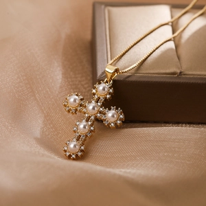 Collana a croce placcata oro con perle e zirconi su sfondo in seta morbida