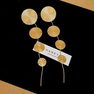 Detailed view of long gold tassel earrings with textured circular plates on black velvet