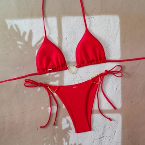 Red bikini set with gold heart rings and side-tie bottoms on a textured background