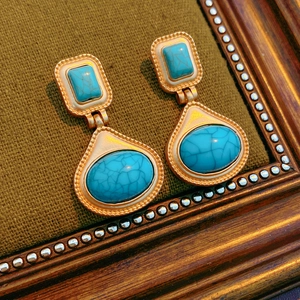 Macro view of vintage gold earrings with sky blue resin stones on green fabric