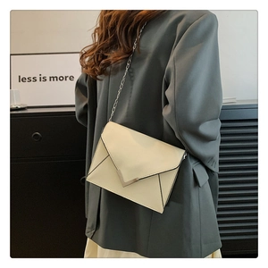 Close-up of cream envelope chain bag with V-shaped metal buckle and leather texture