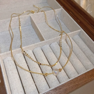 Detail of layered gold snake chain necklace with iridescent pearl charm in a velvet box
