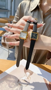 Elegant gold square watch set with leather straps on a wrist in an outdoor setting