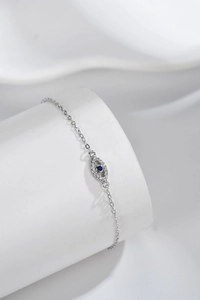 Detailed view of silver evil eye bracelet with blue gemstone on white silk background