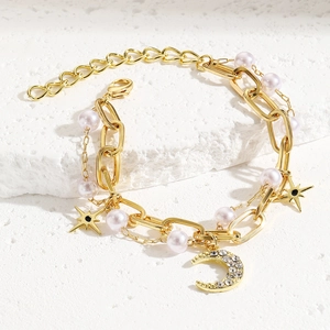 Detail of layered gold bracelet with baroque pearls, star charms, and moon pendant