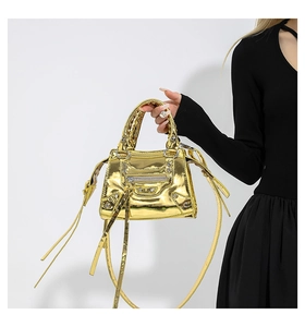 Detail of metallic gold patent handbag with rivets and tassels worn by a model
