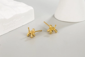 Macro detail of high-polish gold balloon dog stud earring on white geometric prop