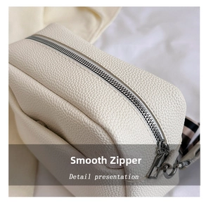 Close-up of smooth metal zipper and white pebbled leather texture on a shoulder bag