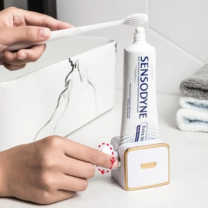 Manual white toothpaste squeezer with gold trim on white washstand for bathroom