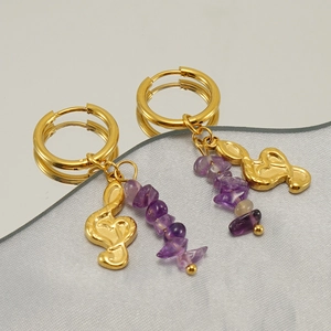 Detail der goldenen Creolen mit lila Natursteinperlen und Notenschlüssel-Anhängern im Fokus
