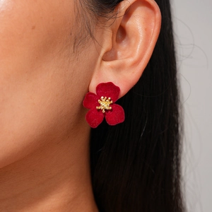 Gros plan d'une boucle d'oreille fleur rouge floquée avec cœur doré sur l'oreille