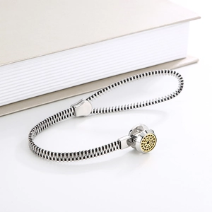 Macro shot of silver zipper-style bracelet with a gold sun pendant on a book edge
