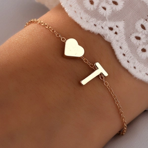 Bracelet doré pour femme avec pendentifs cœur et lettre T sur fond de dentelle blanche