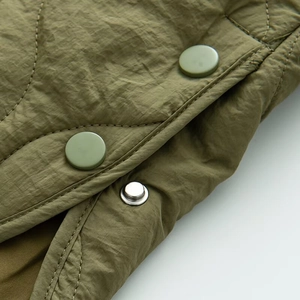 Detail der armygrünen Steppjacke mit runden Druckknöpfen und Nylon-Textur-Oberfläche