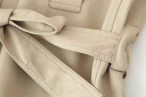Detailed close-up of khaki trench coat belt knot showing fine stitching and fabric texture