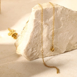 Élégant collier avec pendentif rose 3D plaqué or 18K présenté sur un fond de pierre blanche