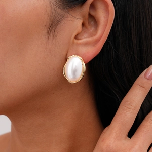 Gros plan d'une grande boucle d'oreille perle ovale avec monture dorée irrégulière