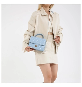 Détail du sac bandoulière matelassé bleu clair avec fermoir doré porté par un modèle