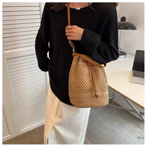 Detail of hand-woven straw bucket bag with brown leather strap worn by a model