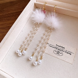 Detail of red bead and white pompom drop earrings with elegant gold tassels