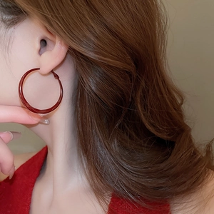 Close-up of a model wearing large glossy burgundy hoop earrings in a twisted design