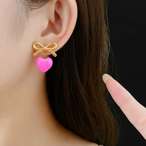 Détail d'une boucle d'oreille nœud doré avec un pendentif cœur rose brillant sur un modèle
